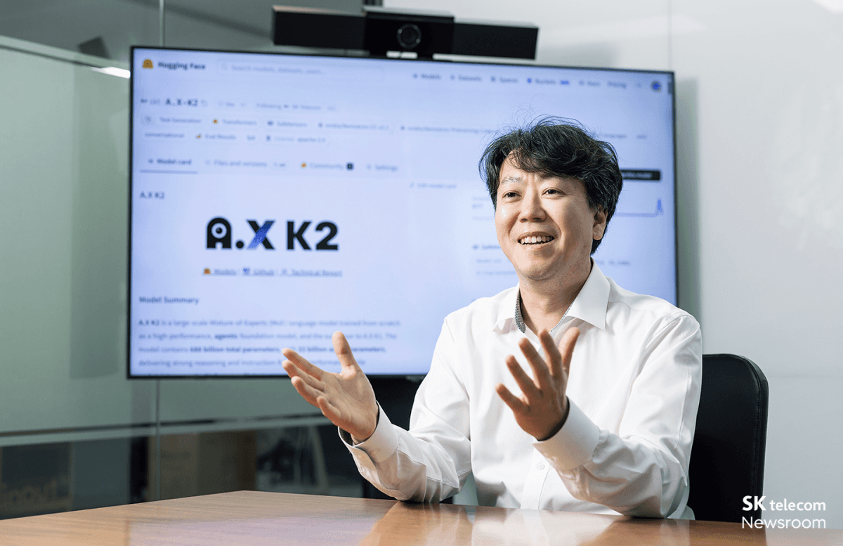 SK텔레콤 뉴스룸에서 촬영된 'A.X K2' 소개 현장. 배경 대형 화면에 허깅페이스에 공개된 A.X K2 모델 카드 페이지가 띄워져 있고, 모델 요약과 매개변수 정보가 표시돼 있다.