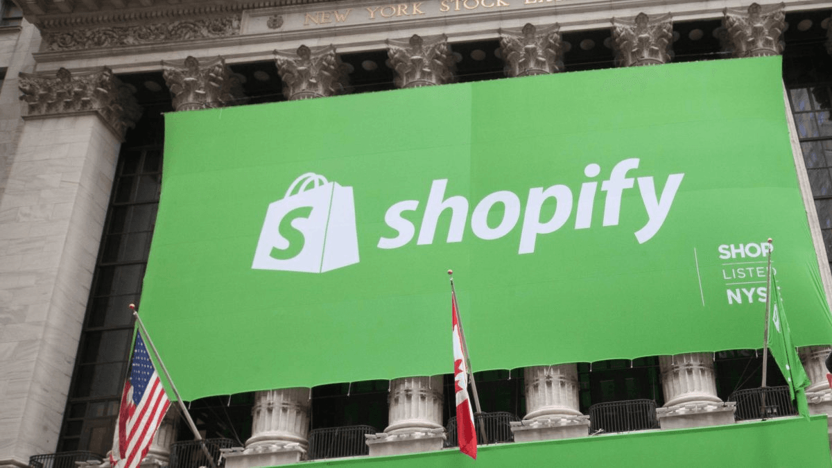 뉴욕증권거래소 건물 외벽에 걸린 대형 초록색 Shopify 배너와 그 아래 성조기·캐나다 국기