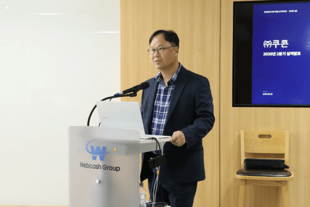 연단에서 마이크를 잡고 발표하는 쿠콘 관계자와 뒤편 화면에 띄운 '㈜쿠콘 2026년 2분기 실적발표' 슬라이드