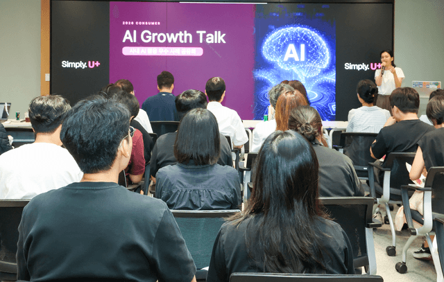LG유플러스 사내 회의실에서 임직원들이 뒷모습으로 앉아 'AI Growth Talk' 발표 화면을 보고 있고, 오른쪽에서 발표자가 마이크를 들고 설명하는 모습