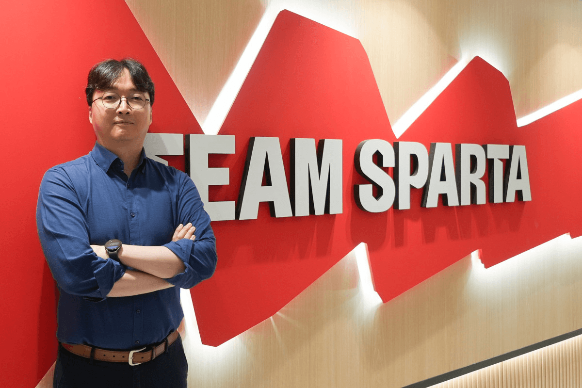 팀스파르타 사옥의 붉은 'TEAM SPARTA' 사인월 앞에서 박영진 AX사업본부장이 팔짱을 끼고 선 인터뷰 사진