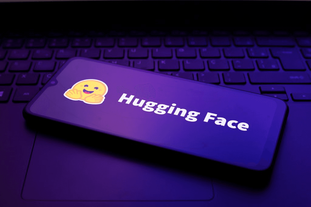 노트북 키보드 위에 놓인 스마트폰 화면에 허깅페이스(Hugging Face) 로고가 떠 있는 모습