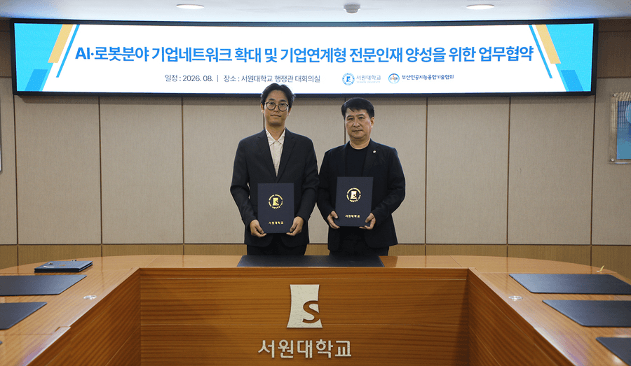 'AI·로봇분야 기업네트워크 확대 및 기업연계형 전문인재 양성을 위한 업무협약' 문구가 적힌 대형 스크린 앞에서 두 사람이 협약서를 펼쳐 들고 선 서원대학교 대회의실 협약식 장면