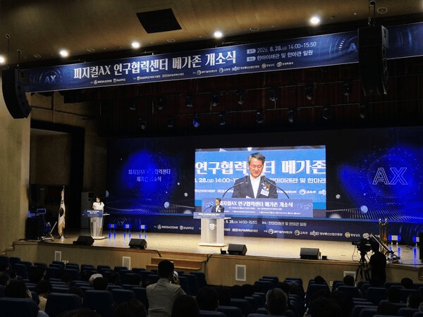 '피지컬AX 연구협력센터 메가존 개소식' 현수막이 걸린 강당 무대에서 관계자가 연단에 서서 발언하고 있고 대형 스크린에 행사 타이틀이 표시돼 있다