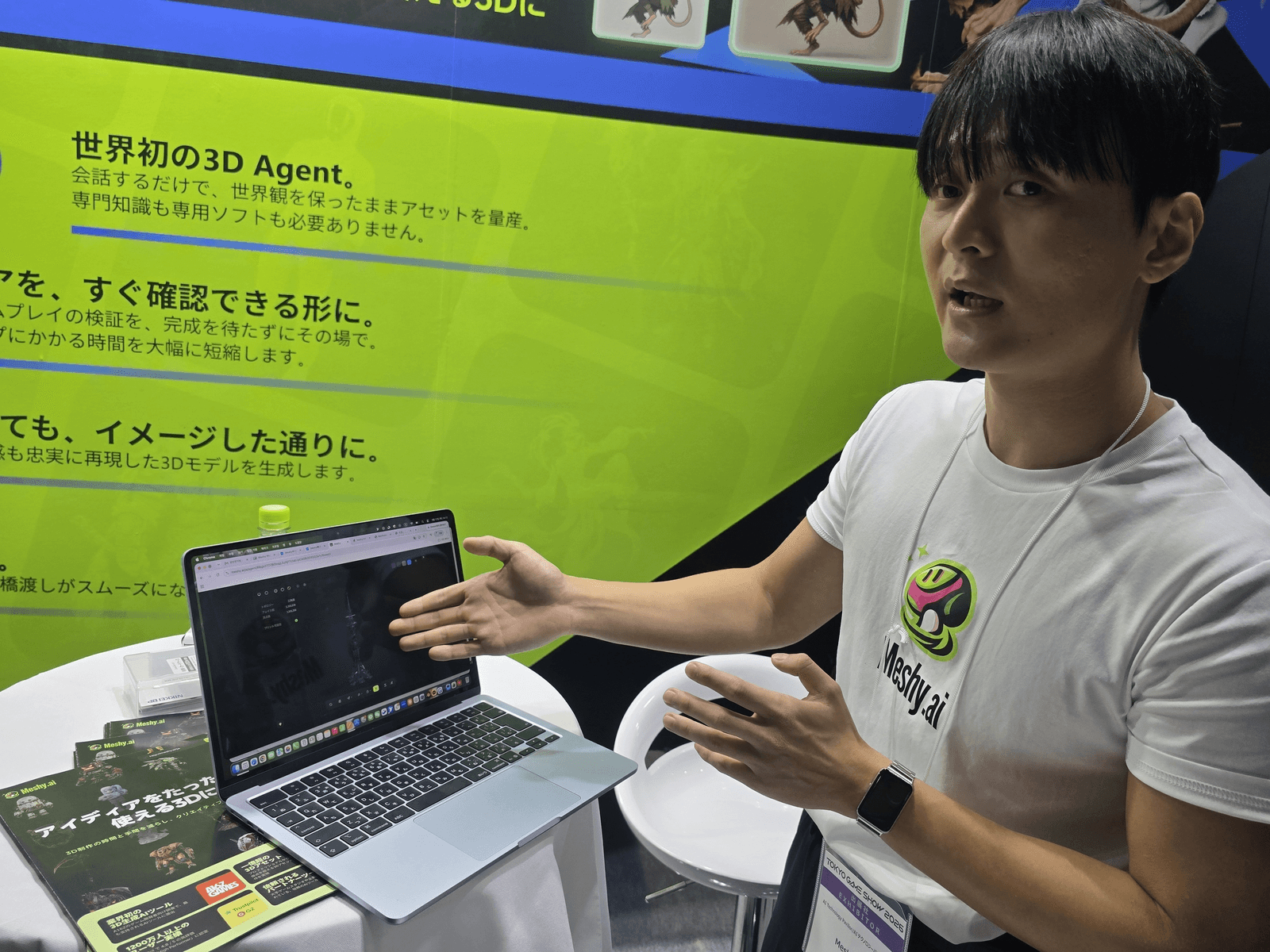 도쿄게임쇼(TGS) 2026 'AI 테크놀로지 파빌리온'의 메시 AI(Meshy.ai) 부스에서 담당자가 노트북으로 3D 모델 생성 데모를 시연하고 있다. 뒤편 전시 패널에 '세계 최초의 3D Agent'라는 일본어 문구가 적혀 있다.