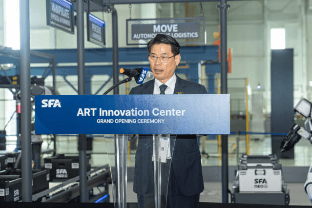 SFA 아산사업장 'ART 이노베이션 센터' 개관식에서 인사말을 하는 모습, 뒤로 물류 자동화 설비가 보인다