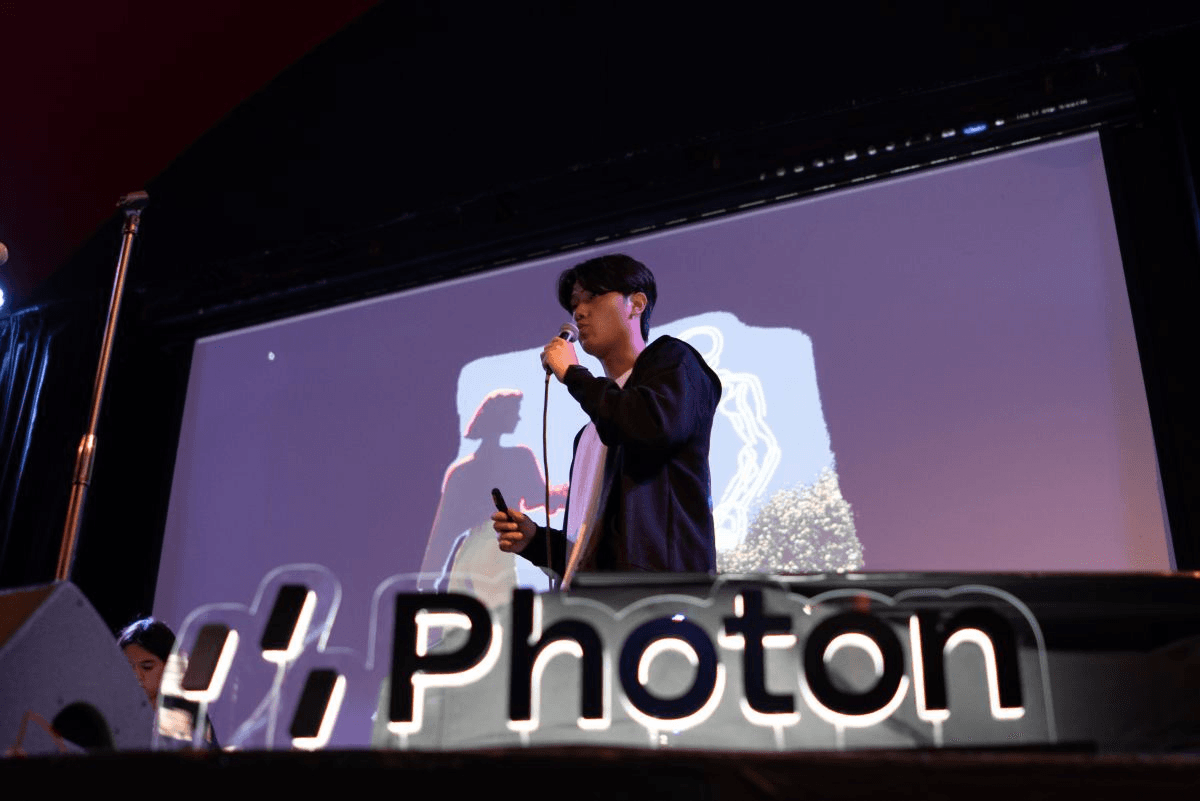 Photon 행사 무대에서 마이크를 들고 발표하는 모습과 Photon 네온 로고