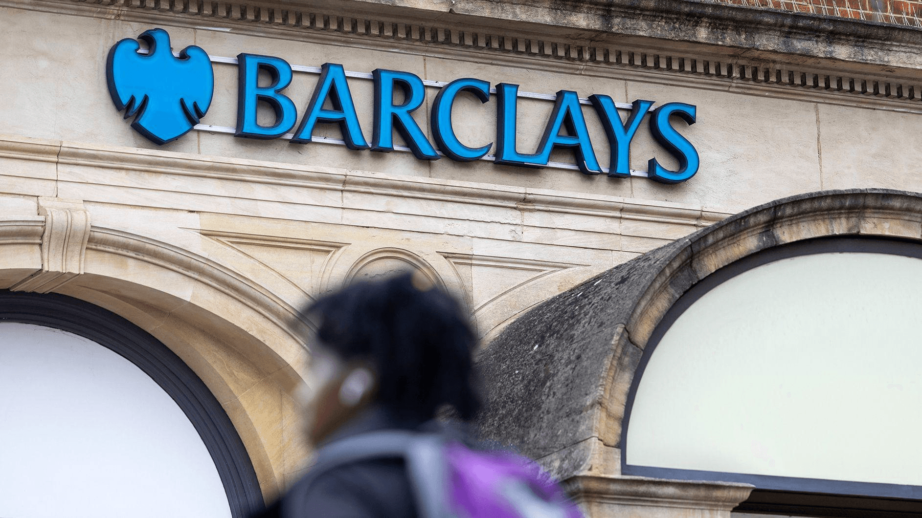 바클레이즈 지점 외벽의 BARCLAYS 간판과 그 앞을 지나가는 행인